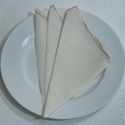 Prato branco com três guardanapos de tecido bege dobrados em leque sobre toalha branca