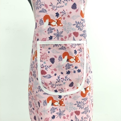 Avental rosa com padrão de raposas castanhas e folhas coloridas com bolso branco.