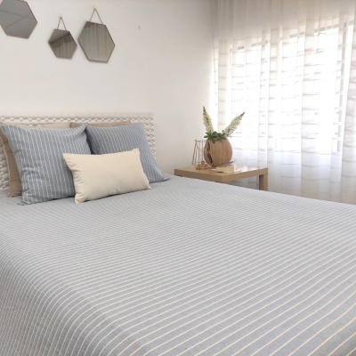 Cama com roupa de cama azul com riscas brancas, almofadas e espelhos hexagonais na parede