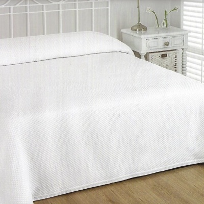 Cama com edredão branco texturizado num quarto iluminado