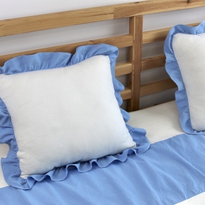 Almofadas brancas com borda azul clara rodada e manta azul clara numa cama de madeira