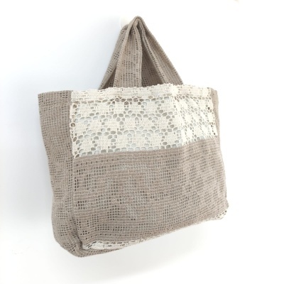 Saco de mão bege com painel rendado branco pendurado na parede branca