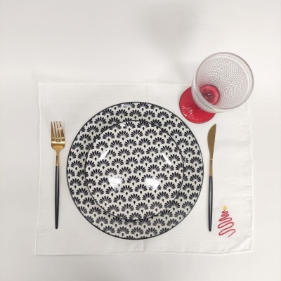 Conjunto de jantar com prato padrão preto e branco, guardanapo branco com bordado natal, talheres pretos e dourados, copo com base vermelha
