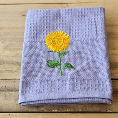 Toalha roxa com bordado de girassol sobre superfície de madeira