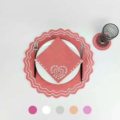 Conjunto de mesa com prato branco, guardanapo rosa com padrão, base ondulada rosa, talheres e copo preto