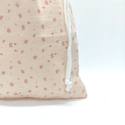 Parte inferior de bolsa em tecido creme com flores pequenas cor-de-rosa e cordão branco.