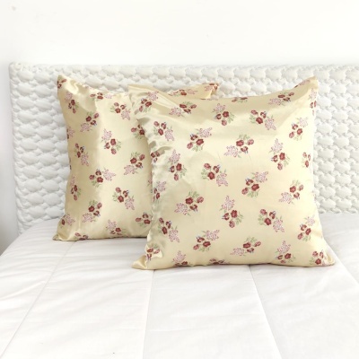 Duas almofadas creme com padrão floral vermelho sobre cama branca