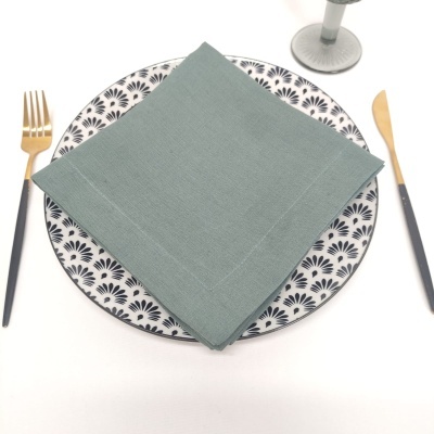 Conjunto de mesa com prato decorado, guardanapo cinza, talheres dourados e pretos, copo de pé ao fundo