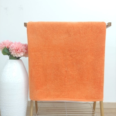 Toalha laranja felpuda pendurada em suporte de madeira com vaso branco e flores cor-de-rosa