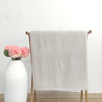 Toalha branca pendurada em suporte de madeira ao lado de vaso branco com flores cor-de-rosa