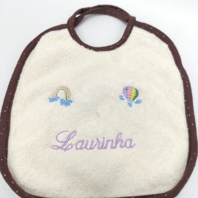 Babete de bebé creme com bordas castanhas e bordados coloridos.