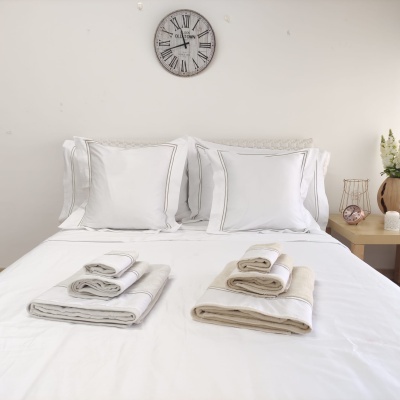 Cama de casal com almofadas brancas e toalhas dobradas, relógio de parede e mesa de cabeceira com decoração