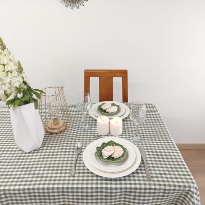 Mesa de jantar com toalha xadrez, pratos com bolachas, velas, vaso com flores e castiçal.