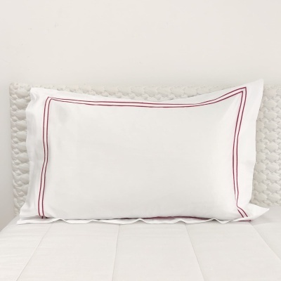 Almofada branca com bordado vermelho numa cama branca.