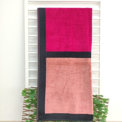 Toalha de banho com padrão geométrico em rosa, vinho e preto pendurada numa estrutura branca