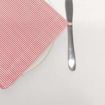 Guardanapo riscado vermelho e branco sobre prato e faca.