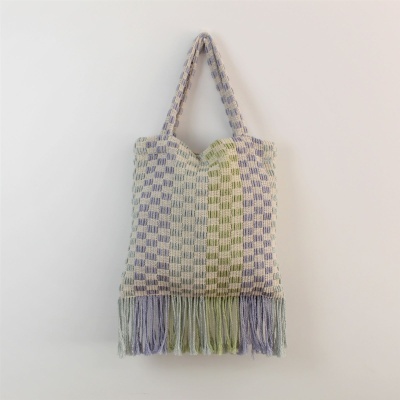 Mala de tecido trançado azul e verde com franjas, pendurada na parede