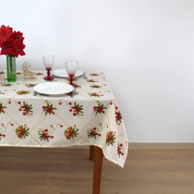 Mesa com toalha creme decorada, pratos brancos, taças de vidro e flores vermelhas na jarra verde