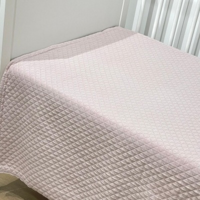 Cobertor rosa claro com padrão de losangos em relevo sobre cama branca