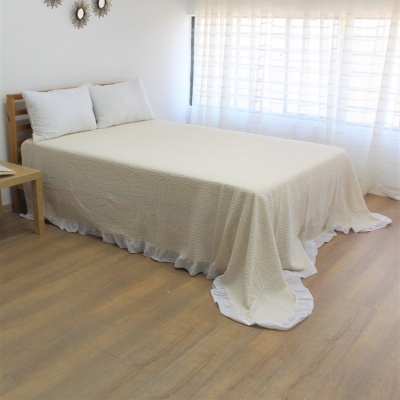 Cama de solteiro com colcha bege texturizada e travesseiros brancos