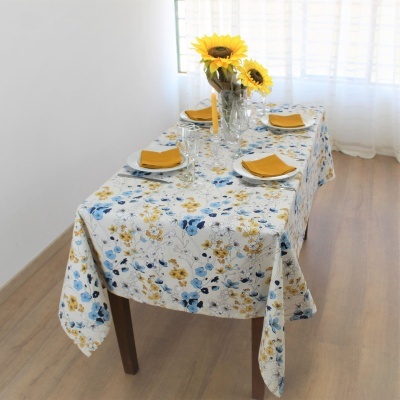 Mesa de jantar com toalha floral, pratos com guardanapos amarelos e vaso com girassóis