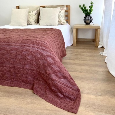 Colcha terracota texturada sobre cama com almofadas neutras e mesa de madeira com vaso preto e planta
