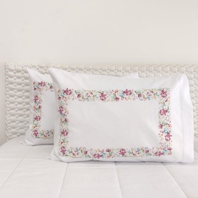 duas fronhas brancas com bordado floral colorido sobre cama branca