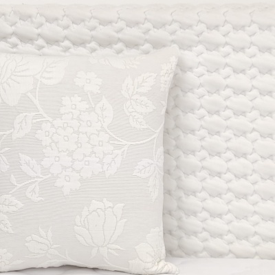 Almofada branca com padrão floral sobre cama branca texturizada