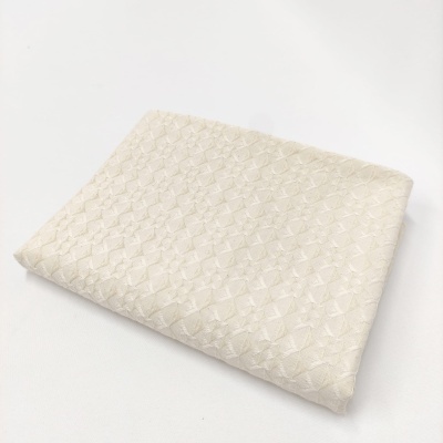 Toalha creme com padrão geométrico em relevo, dobrada sobre superfície branca