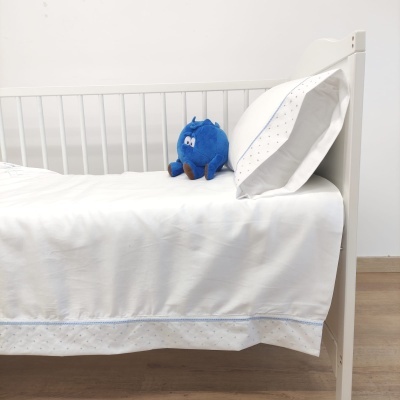 Cama infantil branca com roupa de cama branca e brinquedo azul.