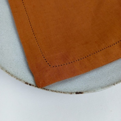 Guardanapo laranja com costuras pretas sobre prato de cerâmica branco