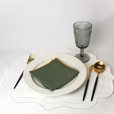 Conjunto de serviço de mesa com prato branco, guardanapo verde escuro, talheres dourados com cabo preto e copo cinza gravado