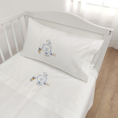 Cama de bebé branca com lençol e fronha bordados com ursinho azul e pássaros amarelos