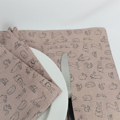 Guardanapos cor de rosa com padrão de animais pequenos em traço preto junto a prato branco e faca