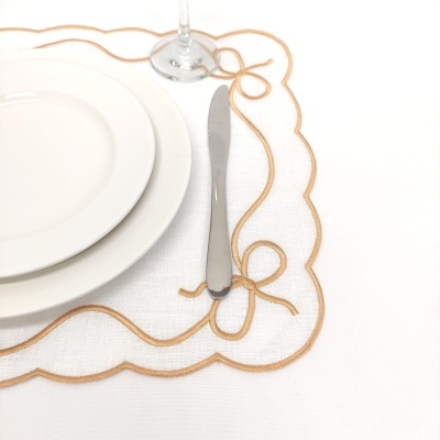 Mesa posta com pratos brancos, faca prateada, copo de pé e toalha branca com bordado dourado
