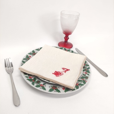 Conjunto de mesa com prato decorado, guardanapo com bordado de rena, talheres metálicos e copo com base vermelha