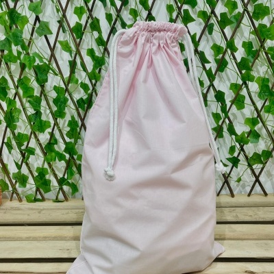 Saco cor-de-rosa com cordão branco sobre madeira e fundo verde