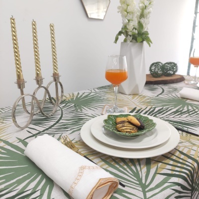 Mesa posta com decoração tropical, pratos, copo com bebida, castiçal com velas e jarro com flores
