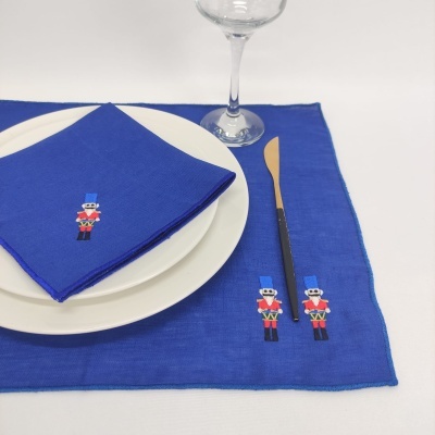 Conjunto de loiça com prato branco, guardanapo azul com bordado e toalha azul com bordados, faca e copo