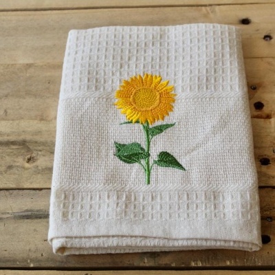 Toalha branca com bordado de girassol sobre madeira
