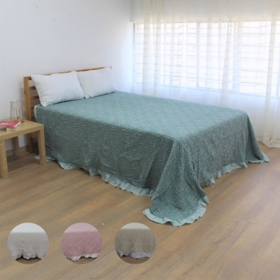 Cama de madeira com colcha azul esverdeada matelassê e almofadas brancas junto a mesa de cabeceira em ambiente iluminado
