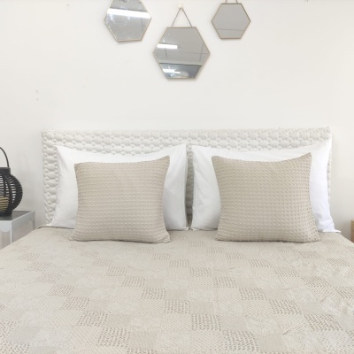 Cama branca com almofadas e edredom bege e espelhos hexagonais na parede