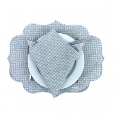 Conjunto de mesa com prato branco, talheres prateados, guardanapo e base de mesa cinza com padrão pied-de-poule.