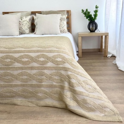 Cama com colcha bege e almofadas brancas, mesa de cabeceira com vaso preto e planta, chão de madeira clara