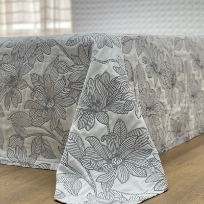 Colcha branca com padrão floral cinzento sobre cama
