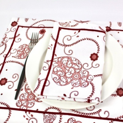 Guardanapos e jogo americano branco com padrão floral vermelho sobre prato branco e garfo preto