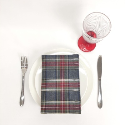 Mesa posta com prato branco, talheres, guardanapo xadrez e copo com base vermelha