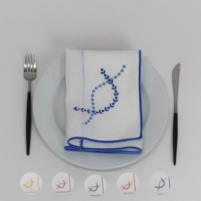 Guardanapo branco com bordado azul sobre prato branco com talheres à esquerda e direita