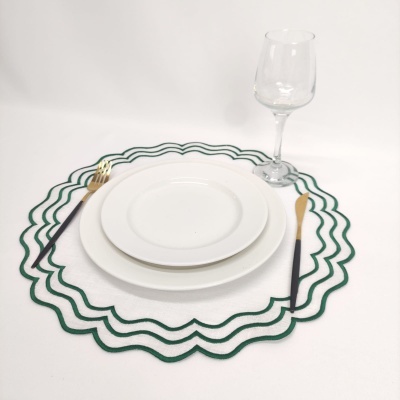 Conjunto de jantar com pratos brancos, talheres dourados e pretos, copo de vinho e bases onduladas verdes e brancas.