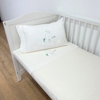 Cama de bebé branca com lençol e almofada bordados com boneco de neve